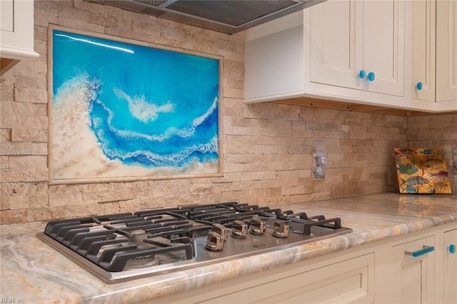 room details with light stone counters, stainless steel gas cooktop, decorative backsplash, white cabinetry, and ventilation hood