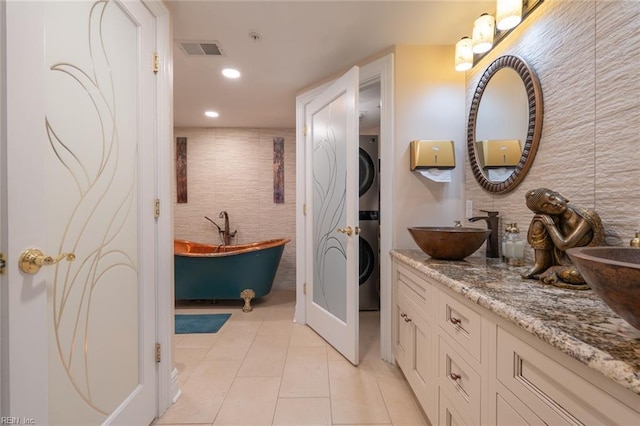 bathroom featuring visible vents, stacked washer and clothes dryer, tile patterned flooring, a freestanding tub, and a sink