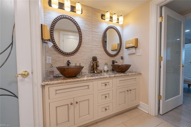 bathroom featuring tasteful backsplash, tile patterned flooring, a sink, and double vanity