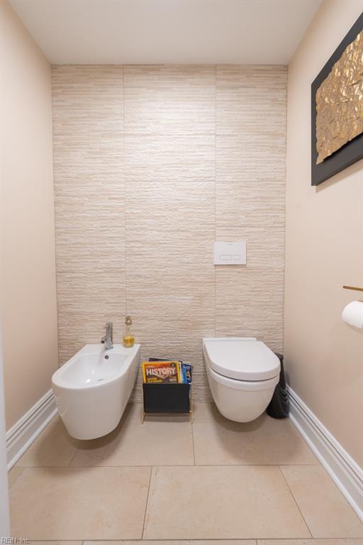 half bathroom with toilet, tile walls, baseboards, tile patterned floors, and a bidet