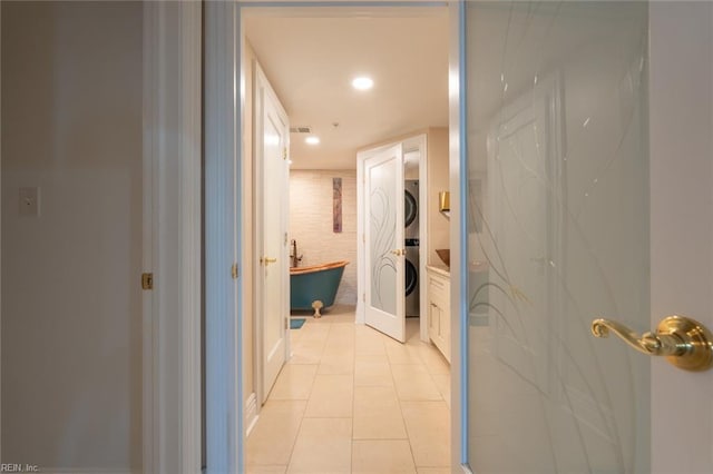 corridor with stacked washer and dryer, light tile patterned flooring, and visible vents