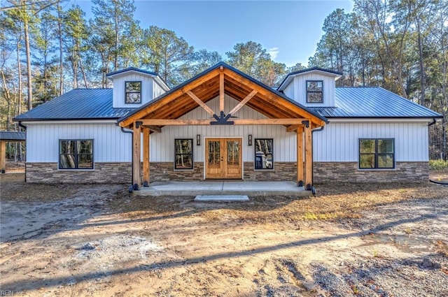 view of front of house with stone siding, french doors, metal roof, and a patio