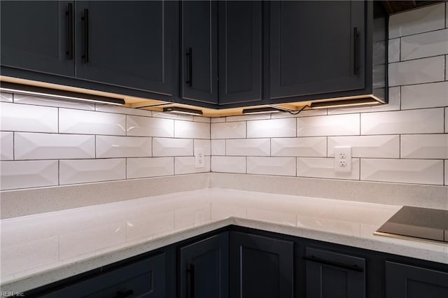 kitchen featuring light stone countertops, black electric stovetop, backsplash, and dark cabinets