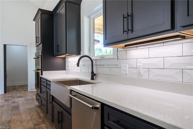 kitchen with dark wood finished floors, decorative backsplash, appliances with stainless steel finishes, light stone counters, and a sink