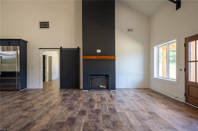 unfurnished living room with dark wood-style flooring, a fireplace, visible vents, a barn door, and high vaulted ceiling