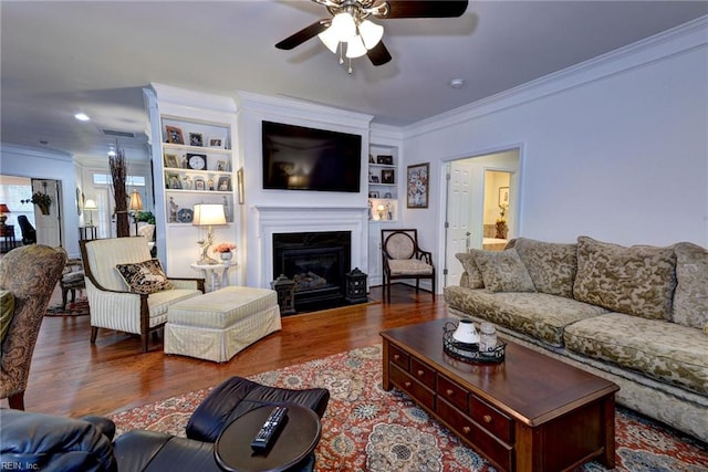 living area featuring a fireplace with flush hearth, ceiling fan, ornamental molding, and wood finished floors