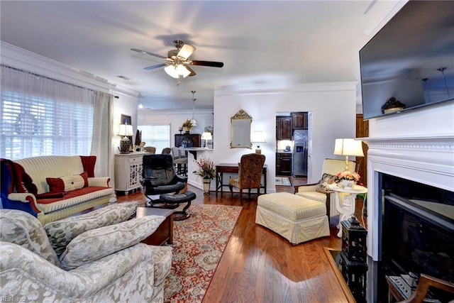 living room with visible vents, a fireplace with flush hearth, ceiling fan, ornamental molding, and wood finished floors