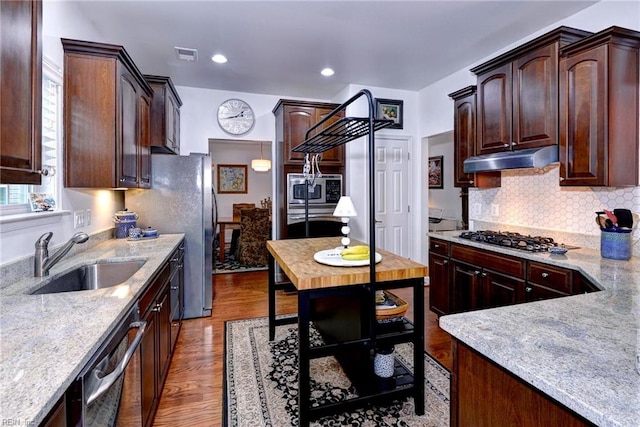 kitchen featuring tasteful backsplash, wood finished floors, stainless steel appliances, under cabinet range hood, and a sink