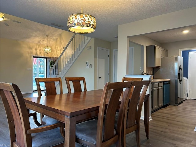 dining space featuring visible vents, a ceiling fan, wood finished floors, stairs, and a textured ceiling