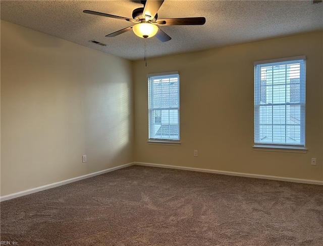 empty room with baseboards, visible vents, ceiling fan, dark colored carpet, and a textured ceiling