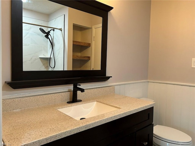 bathroom with a wainscoted wall, toilet, walk in shower, and vanity