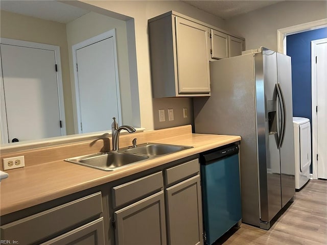 kitchen featuring washer and clothes dryer, dishwashing machine, light countertops, light wood-style floors, and a sink