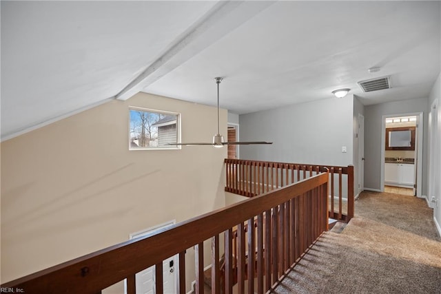 hallway featuring carpet floors, visible vents, lofted ceiling with beams, an upstairs landing, and baseboards