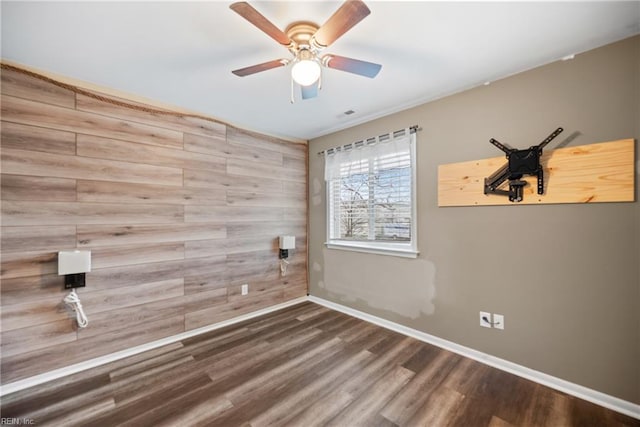 empty room with visible vents, baseboards, a ceiling fan, wood finished floors, and wood walls