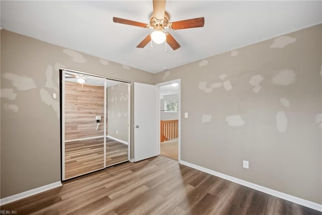 unfurnished bedroom featuring ceiling fan, a closet, baseboards, and wood finished floors