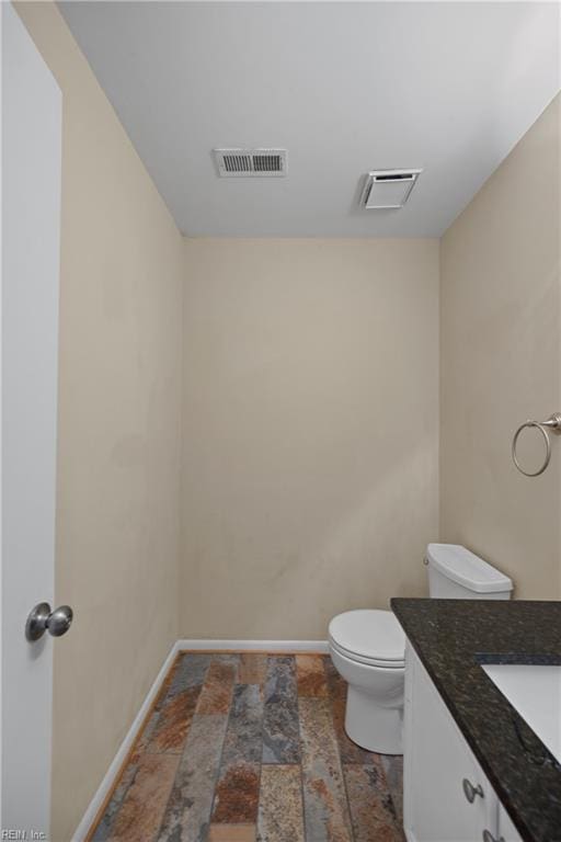 bathroom featuring toilet, vanity, visible vents, and baseboards