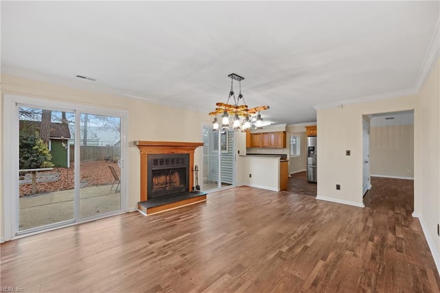 unfurnished living room with baseboards, a fireplace with raised hearth, wood finished floors, crown molding, and a notable chandelier