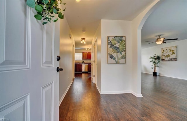 hallway with arched walkways, dark wood-style flooring, and baseboards