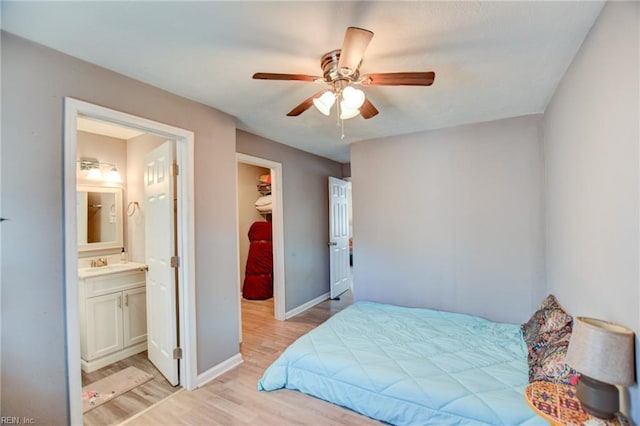 bedroom with light wood finished floors, baseboards, ensuite bath, a spacious closet, and a sink