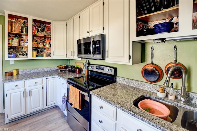 kitchen with appliances with stainless steel finishes, white cabinets, a sink, and light stone counters