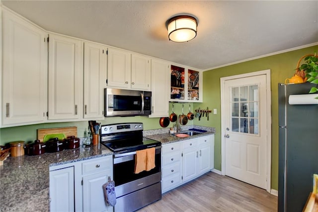 kitchen with dark stone counters, appliances with stainless steel finishes, a sink, and white cabinetry