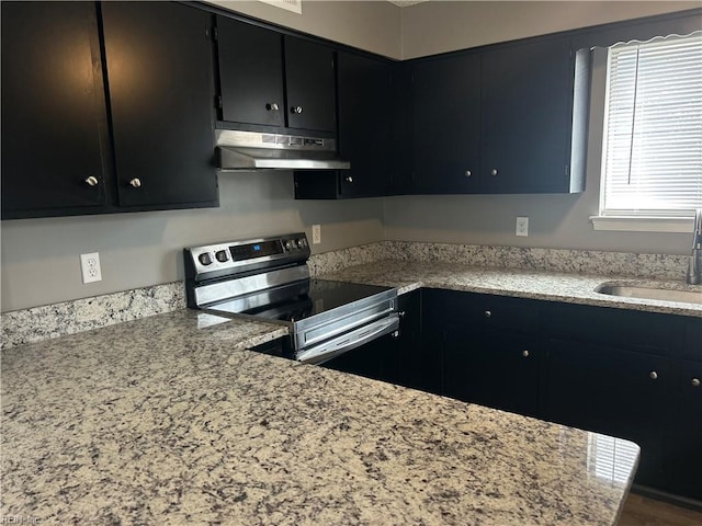 kitchen featuring under cabinet range hood, dark cabinets, a sink, and stainless steel electric stove