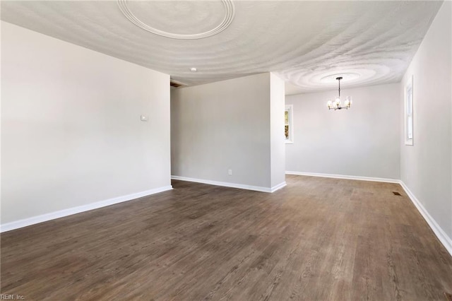 empty room with dark wood-style floors, a chandelier, and baseboards