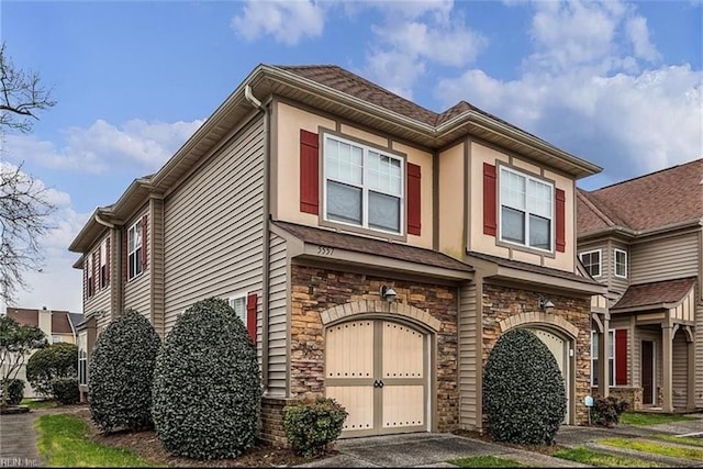 townhome / multi-family property featuring a garage, stone siding, and aphalt driveway