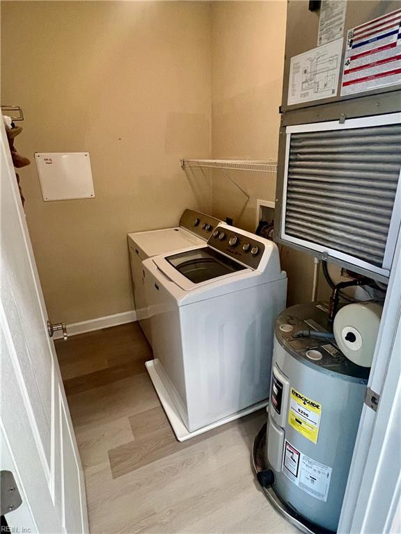 clothes washing area featuring water heater, washing machine and dryer, wood finished floors, laundry area, and baseboards