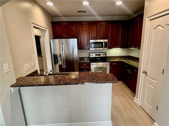 kitchen featuring visible vents, appliances with stainless steel finishes, dark brown cabinets, light wood-type flooring, and a peninsula