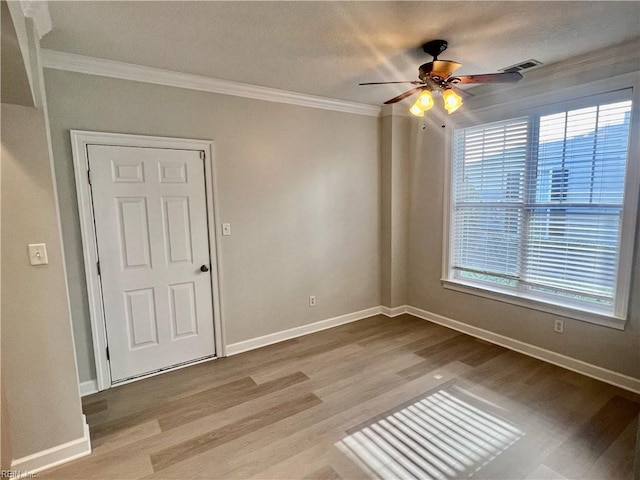 spare room with ornamental molding, a wealth of natural light, baseboards, and wood finished floors