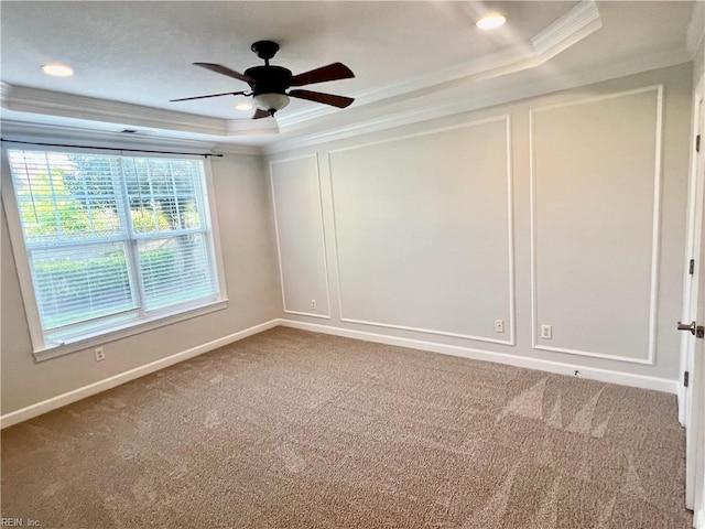 carpeted spare room with baseboards, a ceiling fan, ornamental molding, a tray ceiling, and a decorative wall