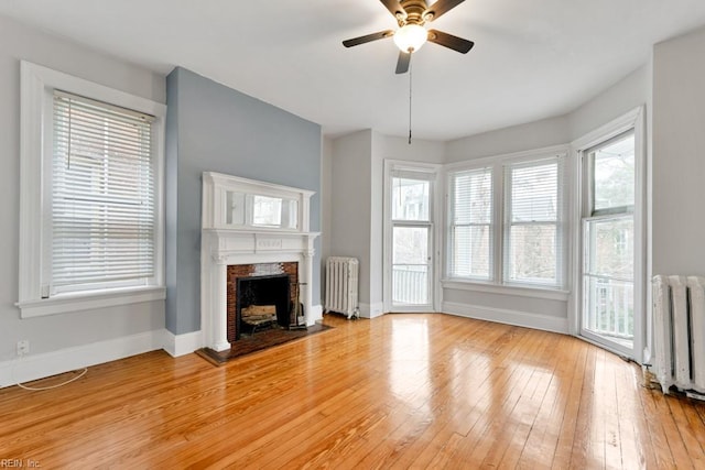 unfurnished living room featuring radiator, light wood-type flooring, a fireplace, and baseboards