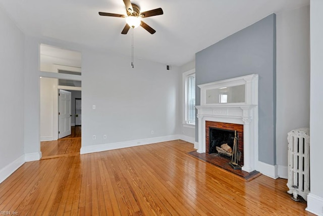 unfurnished living room with light wood-type flooring, a brick fireplace, radiator, and baseboards