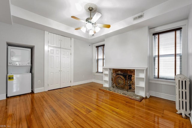 unfurnished living room featuring stacked washer and dryer, visible vents, radiator, a stone fireplace, and light wood-style floors