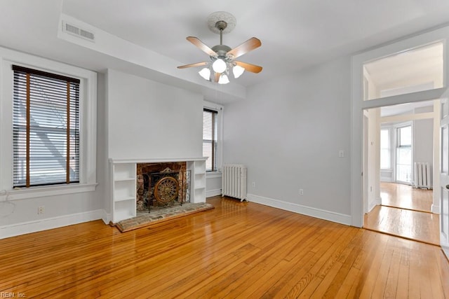 unfurnished living room with baseboards, a fireplace with raised hearth, light wood-style flooring, and radiator heating unit