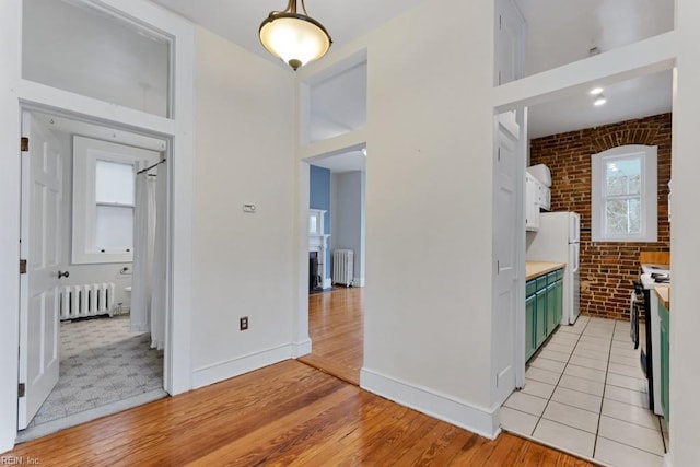 kitchen with brick wall, radiator heating unit, green cabinetry, and electric stove