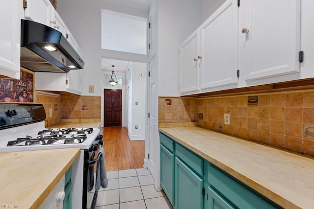 kitchen with light tile patterned floors, tasteful backsplash, white cabinets, gas range, and under cabinet range hood