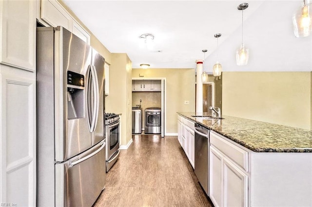 kitchen featuring washing machine and clothes dryer, stainless steel appliances, a sink, wood finished floors, and dark stone counters