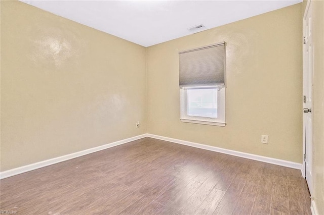 empty room featuring wood finished floors, visible vents, and baseboards