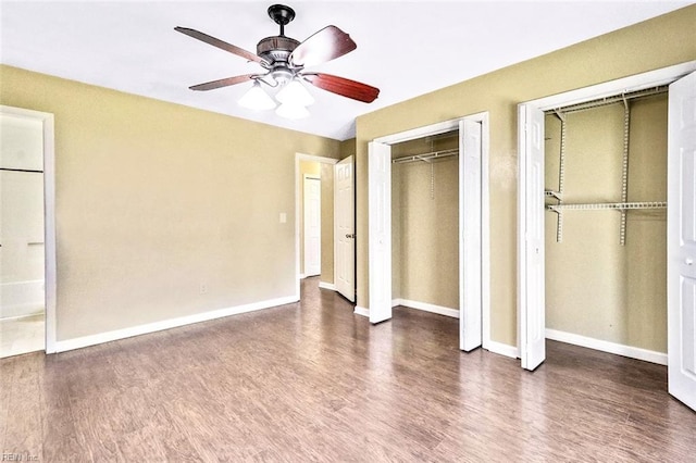 unfurnished bedroom featuring ceiling fan, baseboards, two closets, and wood finished floors