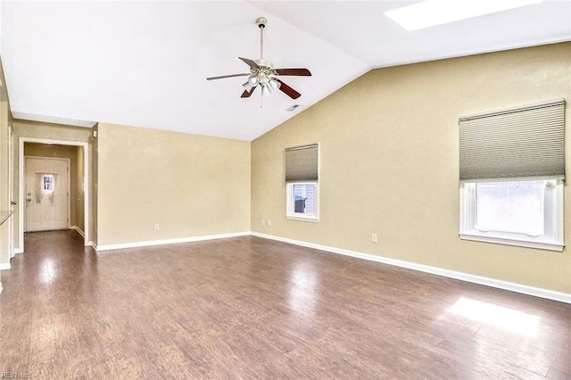 empty room with a ceiling fan, vaulted ceiling with skylight, baseboards, and wood finished floors