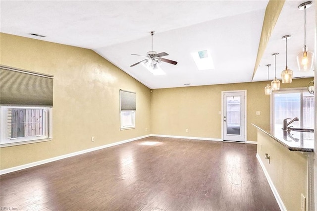 unfurnished living room featuring vaulted ceiling with skylight, dark wood-type flooring, a ceiling fan, visible vents, and baseboards