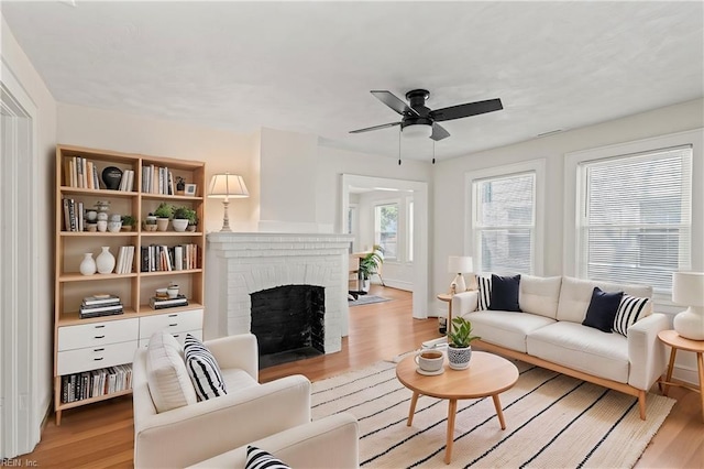 living room featuring a ceiling fan, a brick fireplace, and light wood-style flooring