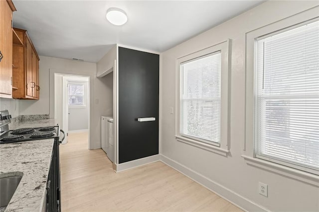 kitchen featuring light wood-style flooring, electric range, brown cabinetry, washer and dryer, and baseboards