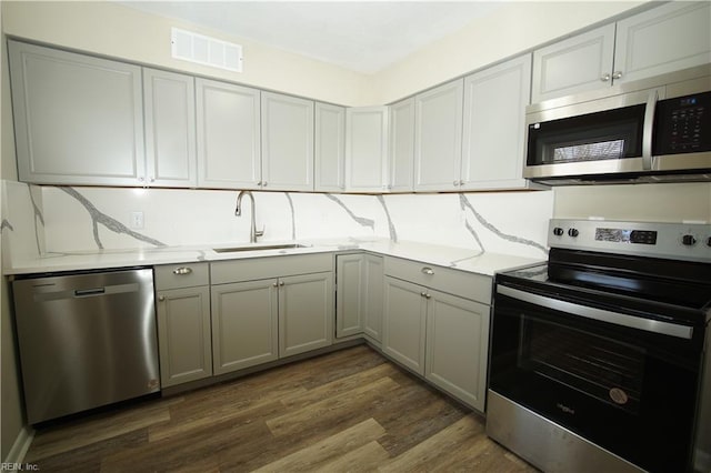 kitchen with gray cabinetry, a sink, visible vents, appliances with stainless steel finishes, and dark wood finished floors