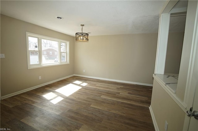 empty room featuring dark wood-style floors, visible vents, baseboards, and a notable chandelier