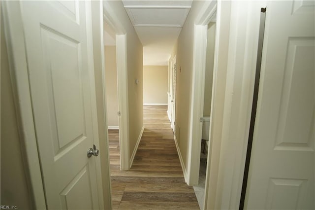 hall featuring attic access, baseboards, and wood finished floors