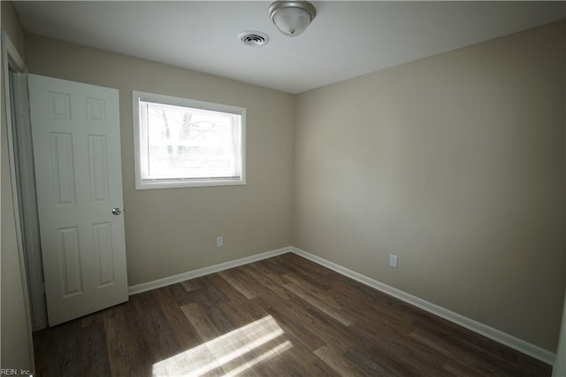 empty room featuring visible vents, dark wood finished floors, and baseboards