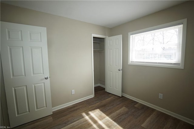 unfurnished bedroom featuring dark wood-type flooring, a closet, and baseboards